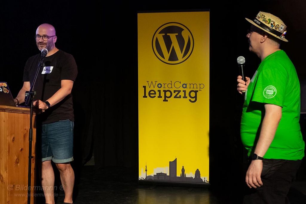 Matthias Pfefferle wird von Robert Windisch anmoderiert, in der Mitte ist unser WordCamp Leipzig RollUp sichtbar